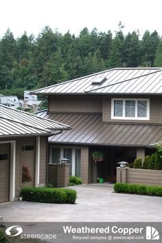 a brown house with metal roofing and trees in the background