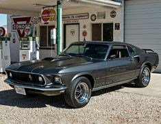 an old mustang parked in front of a gas station