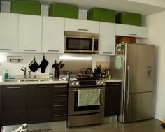 a kitchen with stainless steel appliances and white cupboards, green bins above the sink