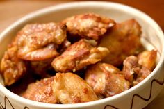 a white bowl filled with chicken wings on top of a wooden table