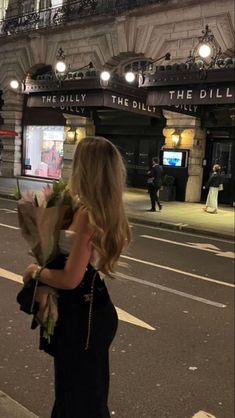 a woman walking down the street with flowers in her hand