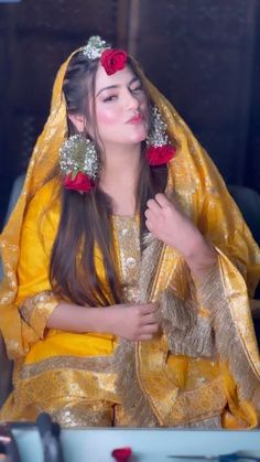 a woman with long hair wearing a yellow dress and red flowers in her hair is sitting down