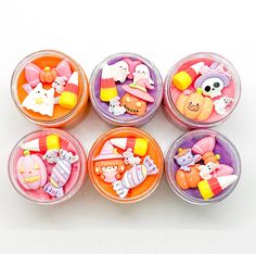 six plastic containers filled with different types of candies on top of a white surface