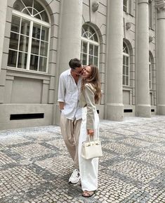 a man and woman kissing in front of a large building with columns on either side