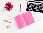 an open laptop computer sitting on top of a white desk next to a pink notebook