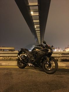 a black motorcycle parked under a bridge at night with city lights in the back ground