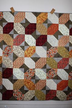 a patchwork quilt hanging on the wall with some brown and orange squares around it