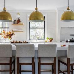 a kitchen with white counter tops and gold pendant lights hanging over the bar stools