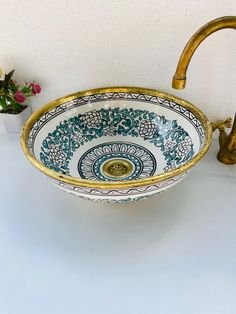 an ornate blue and white bowl with gold rim sits on a counter next to a faucet