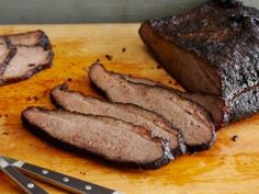 sliced up meat sitting on top of a cutting board next to knifes and fork