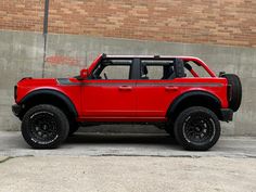 a red truck parked in front of a brick building with black tires and rims