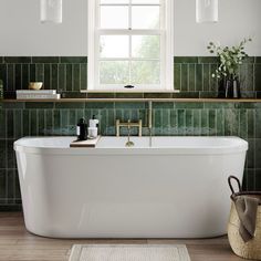 a white bath tub sitting under a window next to a rug and basket with bottles on it