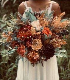 a woman in a white dress is holding a bouquet with orange flowers and greenery