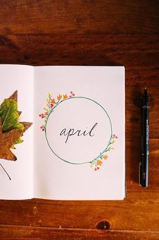 an open book with leaves and the word april written on it next to a pen