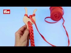 a hand holding a piece of red yarn next to a ball of thread and a wooden heart