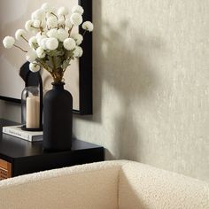 a black vase with white flowers sitting on a table next to a mirror and lamp