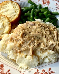 a white plate topped with mashed potatoes and gravy next to green beans