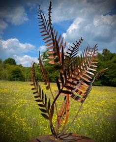 a metal fern sculpture sitting on top of a piece of wood in a grassy field