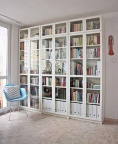 a living room filled with lots of white bookshelves next to a large window