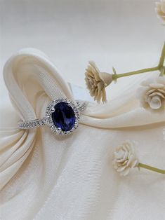 a blue stone ring sitting on top of a white cloth with flowers in the background