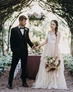 a bride and groom holding hands in front of an arch with greenery on it