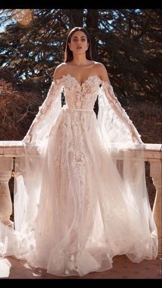 a woman in a wedding dress standing on a bridge with her arms outstretched and wearing an off the shoulder gown