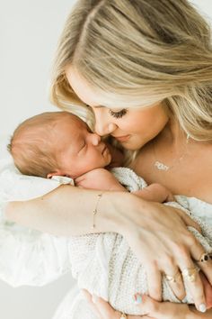 a woman holding a baby in her arms and kissing it's face with both hands