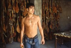 a shirtless man standing in front of some meat