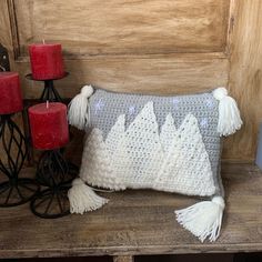 a crocheted pillow sitting on top of a wooden table next to two candles