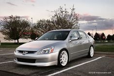 a silver car parked in a parking lot next to some trees and grass at sunset