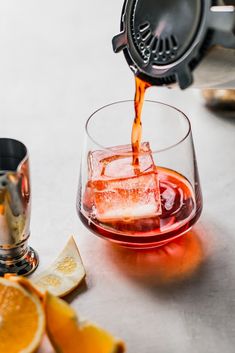 an orange juice being poured into a glass with ice and sliced oranges on the side