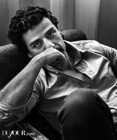 a black and white photo of a man sitting in a chair with his hand on his chin