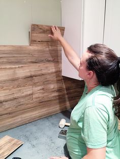 a woman is working on wood planks in a room with white cabinets and flooring