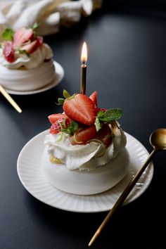 a small cake with strawberries on top is sitting on a plate next to a candle