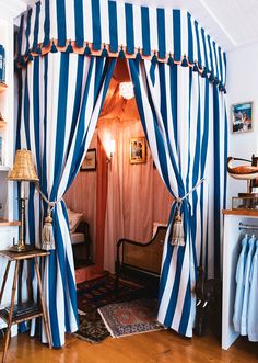 a bedroom with blue and white striped drapes on the ceiling, bed curtains open