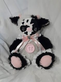 a black and white cow stuffed animal with pink accents on it's face sitting down