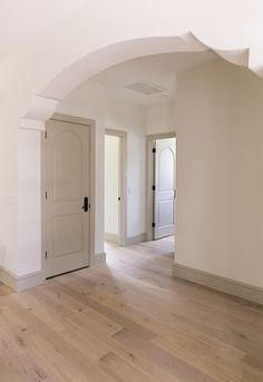 an empty room with white walls and wooden floors, two doors are open to the other side