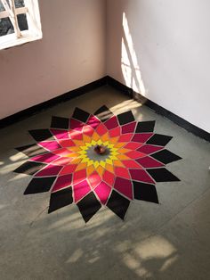 a pink and yellow flower is on the floor in front of a window with sunlight streaming through it