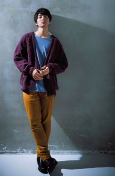 a young man standing in front of a concrete wall with his hands on his hips