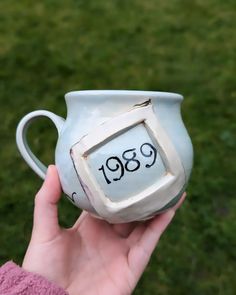 a hand holding a coffee mug with the time 989 on it's side