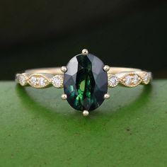 a green and white diamond ring sitting on top of a green surface