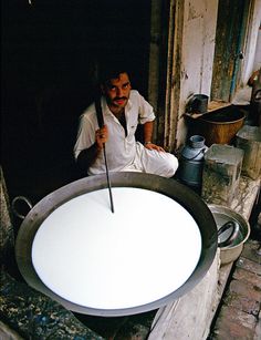 a man sitting in front of a large pan with a knife sticking out of it