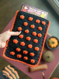 a person holding up a crocheted halloween pumpkin placemat in front of a purple table