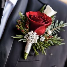 a boutonniere with red roses and greenery is worn by a man in a tuxedo