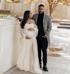 a pregnant woman standing next to a man in a suit and tie near a wall