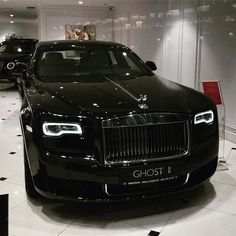 the front of a black car on display in a showroom with other cars behind it