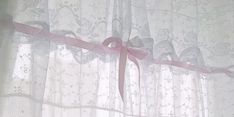 pink ribbon tied to the top of a sheer curtain with lace and bows on it