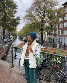 a woman standing on the side of a street next to a river with bicycles parked in front of her