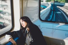 a woman sitting on a train looking out the window at the street below her, with buildings in the background