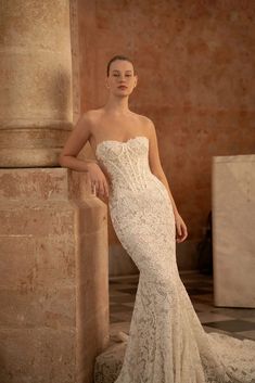 a woman in a wedding dress leaning against a pillar